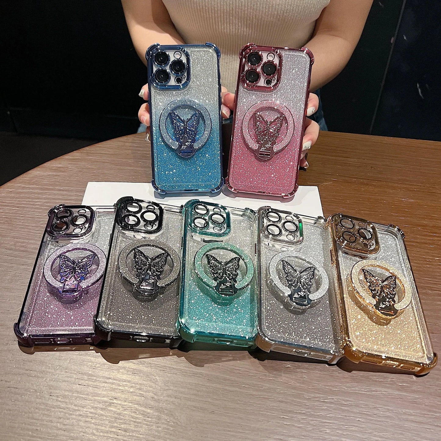 Collection of glittery phone cases with butterfly designs on a wooden surface.