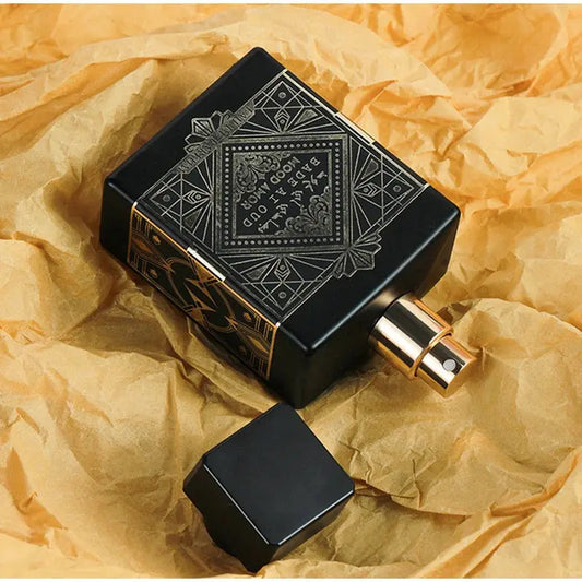 Black perfume bottle with intricate design on a textured yellow surface