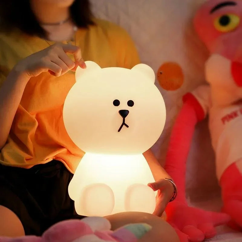 Person holding a bear-shaped night light with a plush toy in the background
