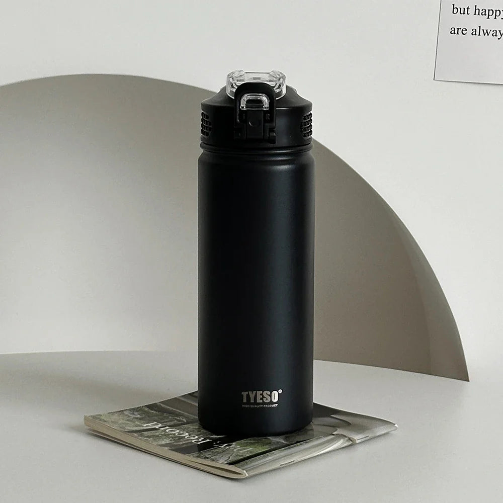 TYESO black thermos bottle with straw on a magazine. Sleek, BPA-free, and insulated for hot or cold drinks.