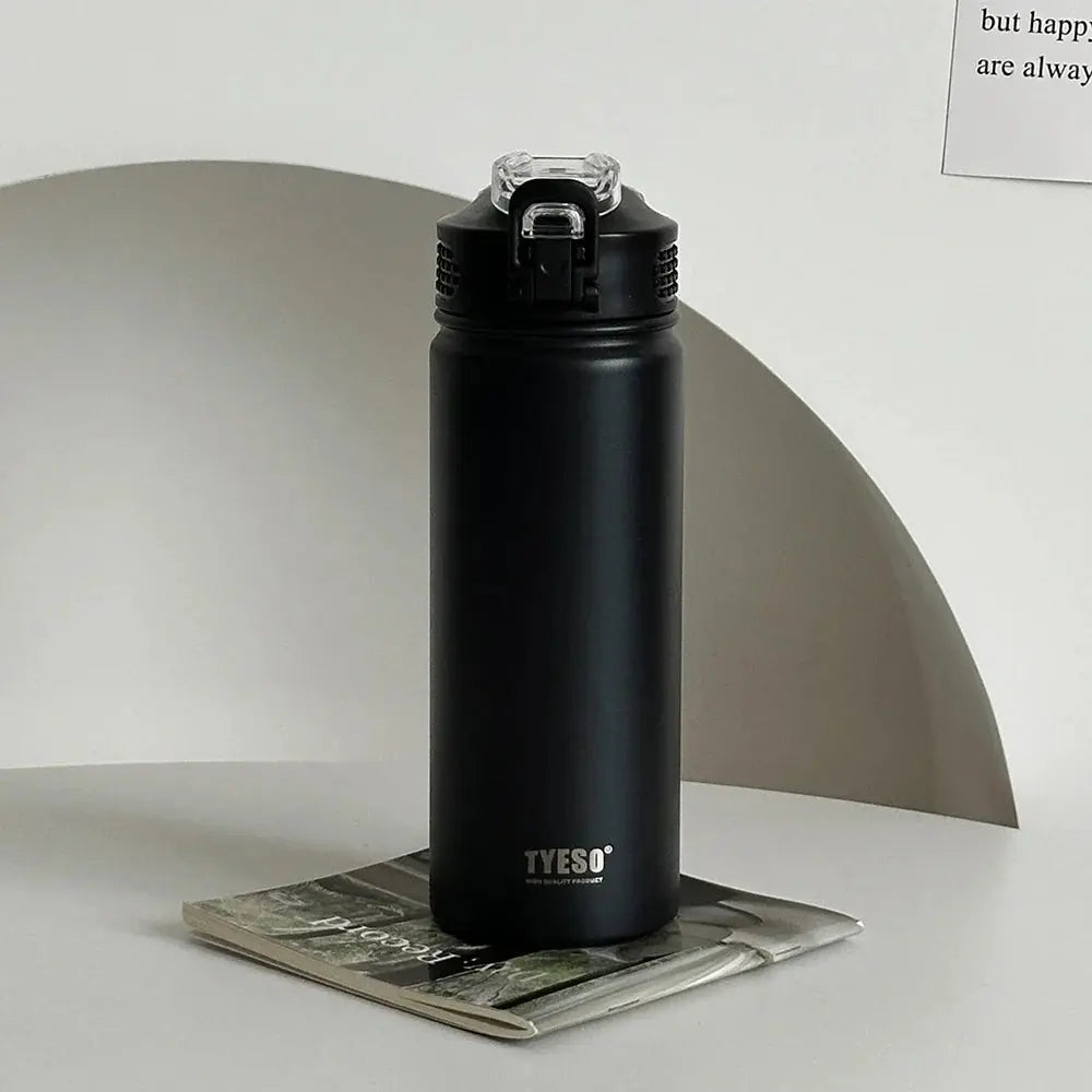 TYESO black thermos bottle with straw on a magazine. Sleek, BPA-free, and insulated for hot or cold drinks.