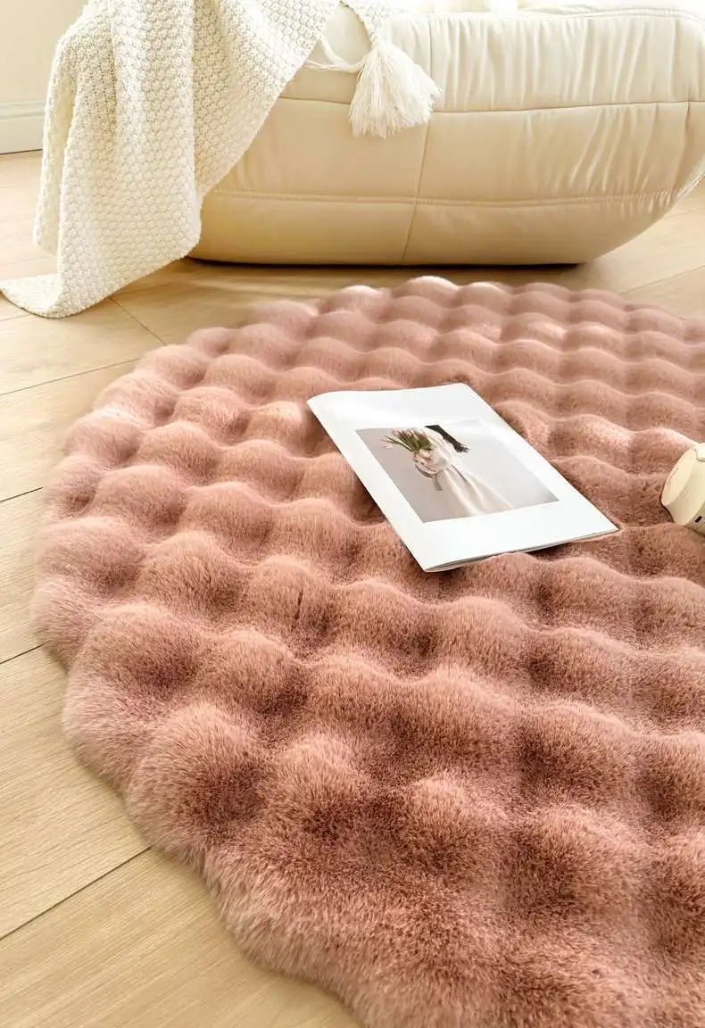 Round pink rug on a wooden floor with a white couch and blanket in the background.