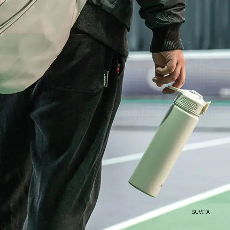 Person holding TYESO white thermos bottle with straw by the loop handle. Ideal for sports, gym, or outdoor activities.
