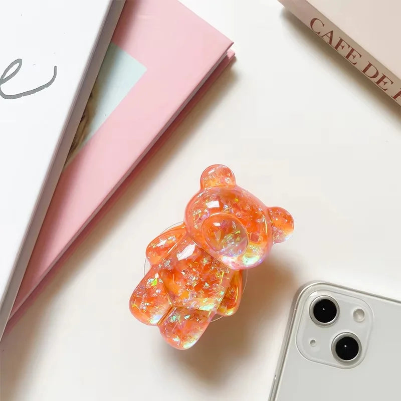 Gummy bear-shaped phone case on a white surface with a pink book and phone visible.