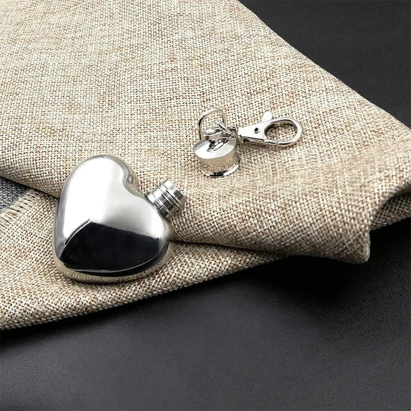 Heart-shaped silver flask with a clip on a textured fabric background