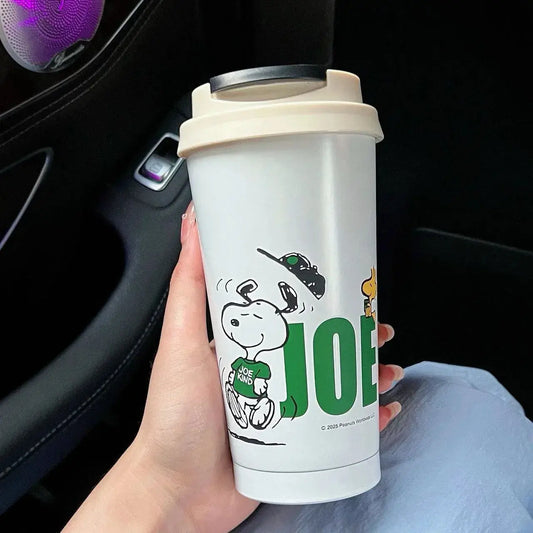 Person holding a Snoopy-themed coffee cup with 'JOE' on it inside a car.