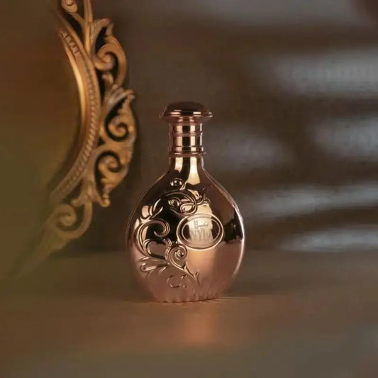 Rose gold bottle with intricate designs on a reflective surface