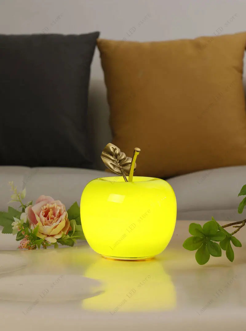 Yellow apple-shaped night light on a surface with flowers and pillows in the background