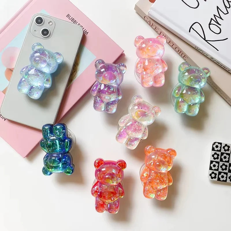 Colorful gummy bear-shaped phone cases on a white surface with books in the background.