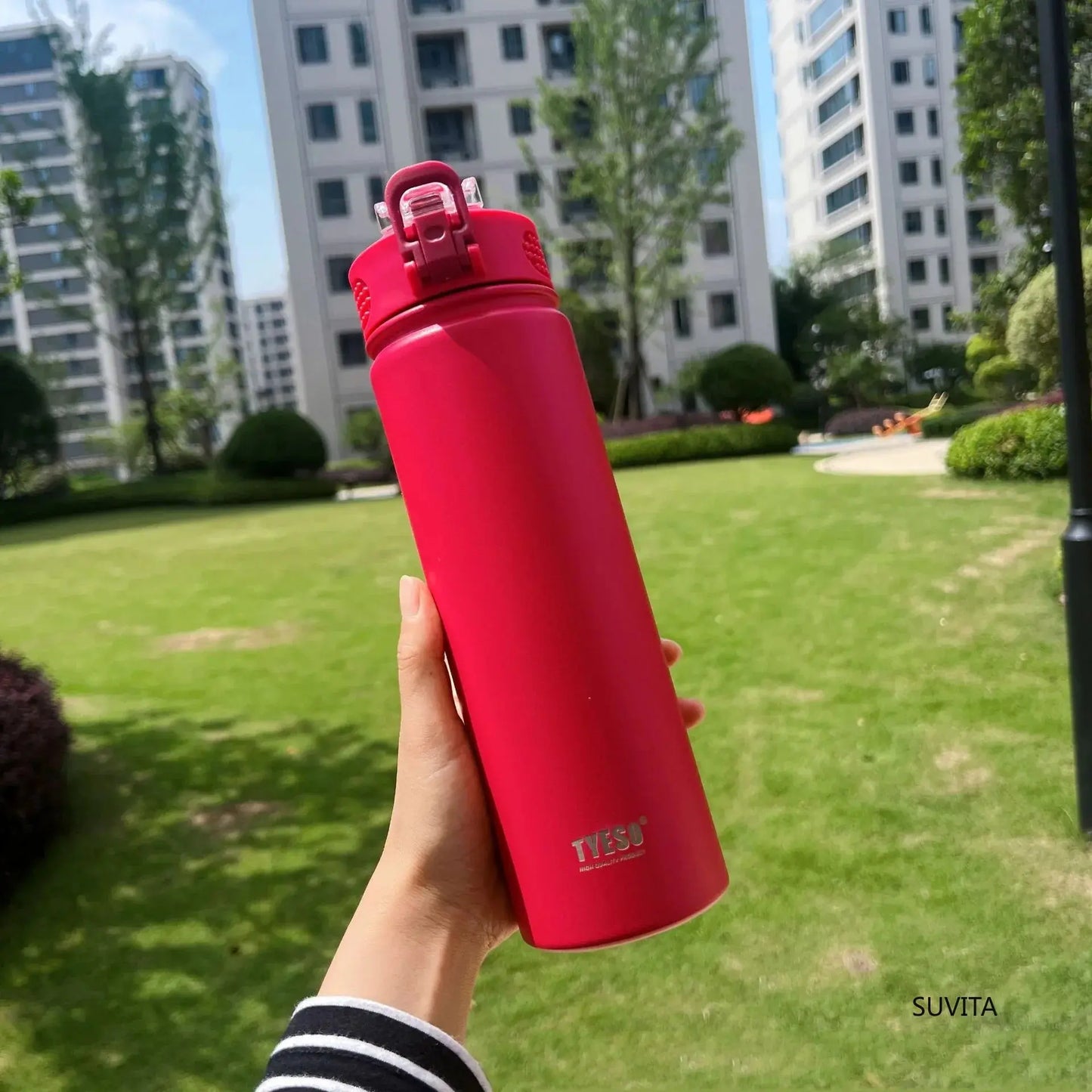 TYESO red thermos bottle with straw held in a park. BPA-free and leak-proof for everyday use.
