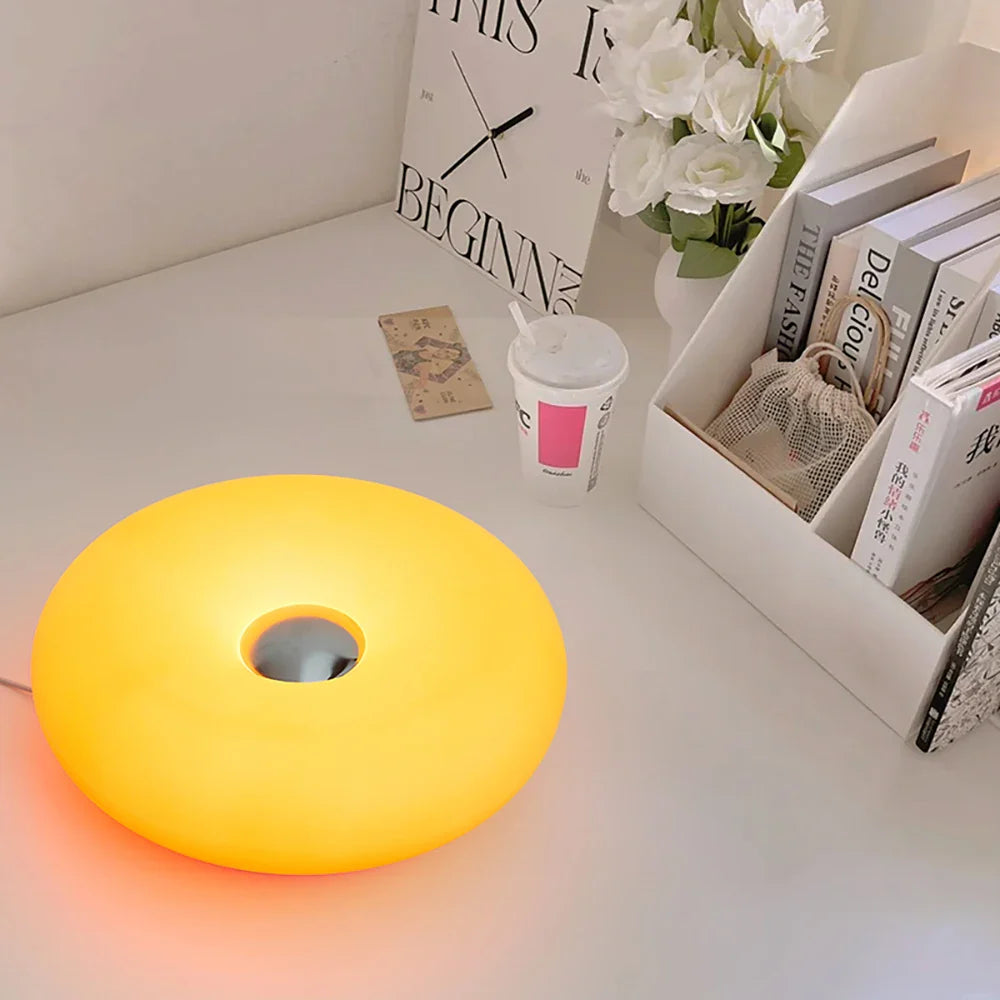 Yellow round lamp on a white surface with books and flowers in the background