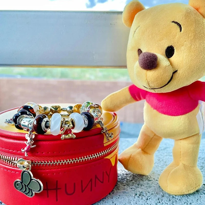 Plush bear next to a red container labeled 'Hunny' with jewelry on a light blue surface. Disney