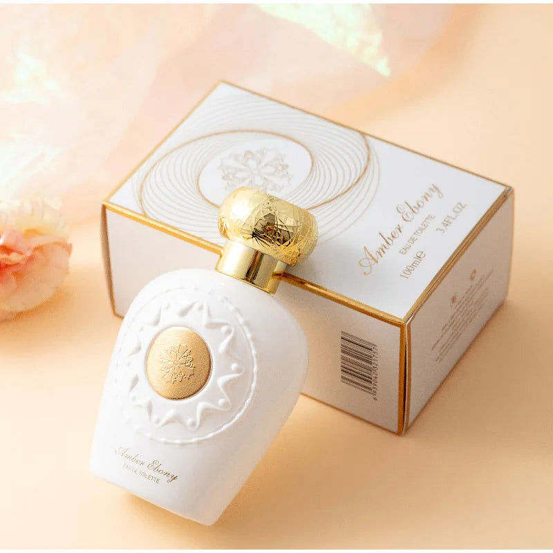 Perfume bottle with gold cap and decorative design next to its packaging on a soft peach background