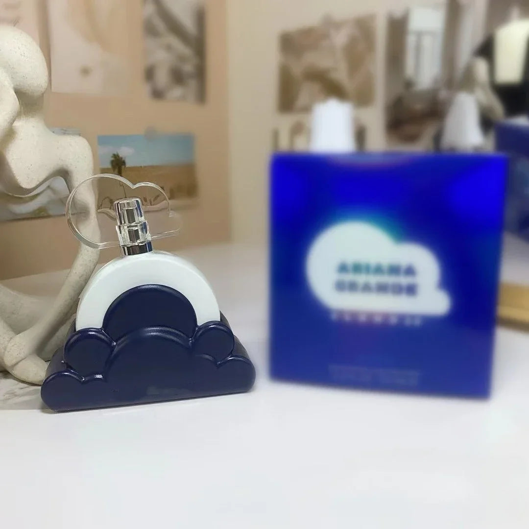 Perfume bottle with blue and white design on a surface, with a blurred Ariana Grande perfume box in the background.