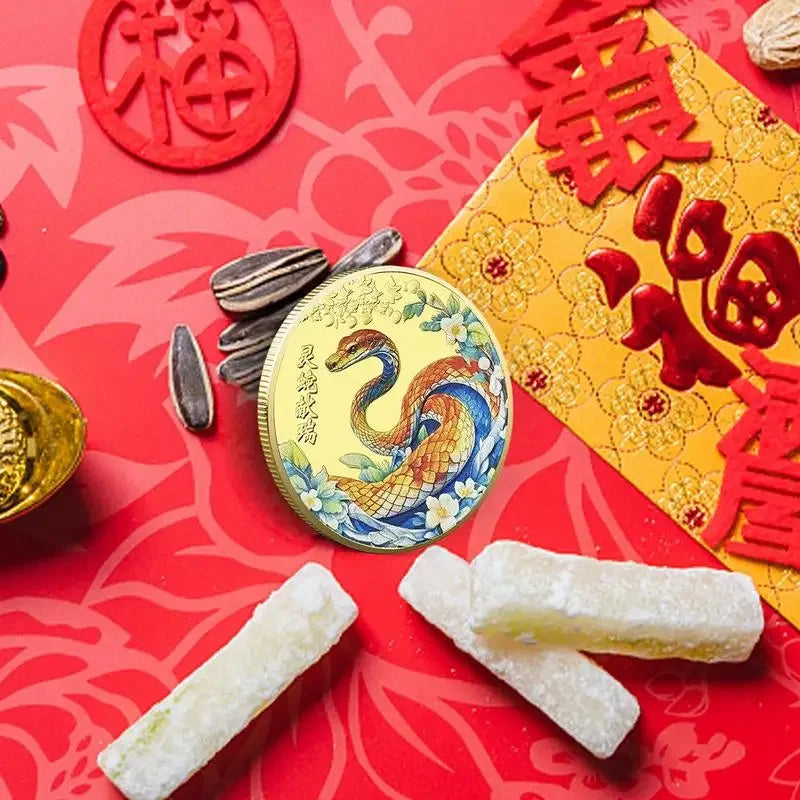 A collectible coin with a 3D relief design of a snake and floral patterns, predominantly in gold and silver colors.