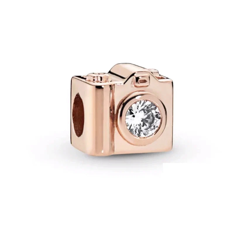 Rose gold camera-shaped charm with a clear gemstone on a white background