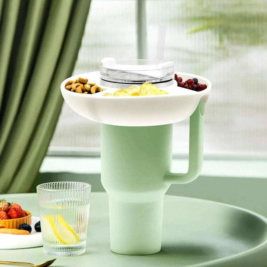 Stanley cup tray White snack tray with food on a green surface, with a glass of water and snacks in the background.