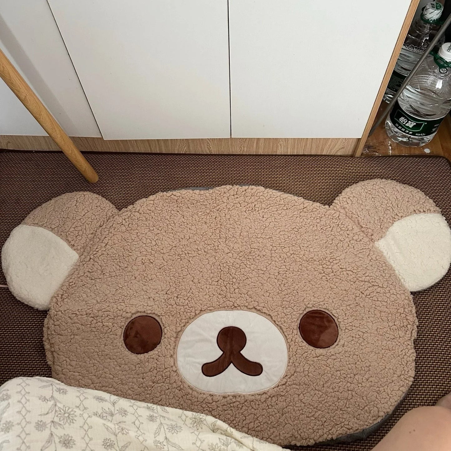 Bear-shaped rug on a floor with a white cabinet and bottles in the background