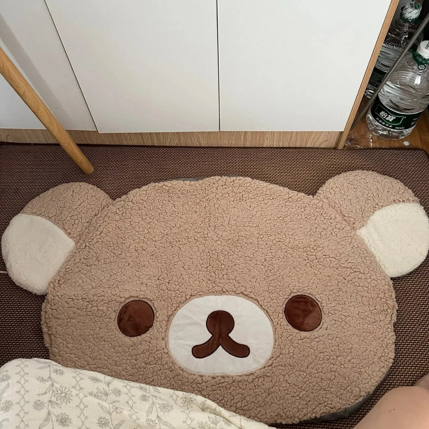 Bear-shaped rug on a floor with a white cabinet and bottles in the background