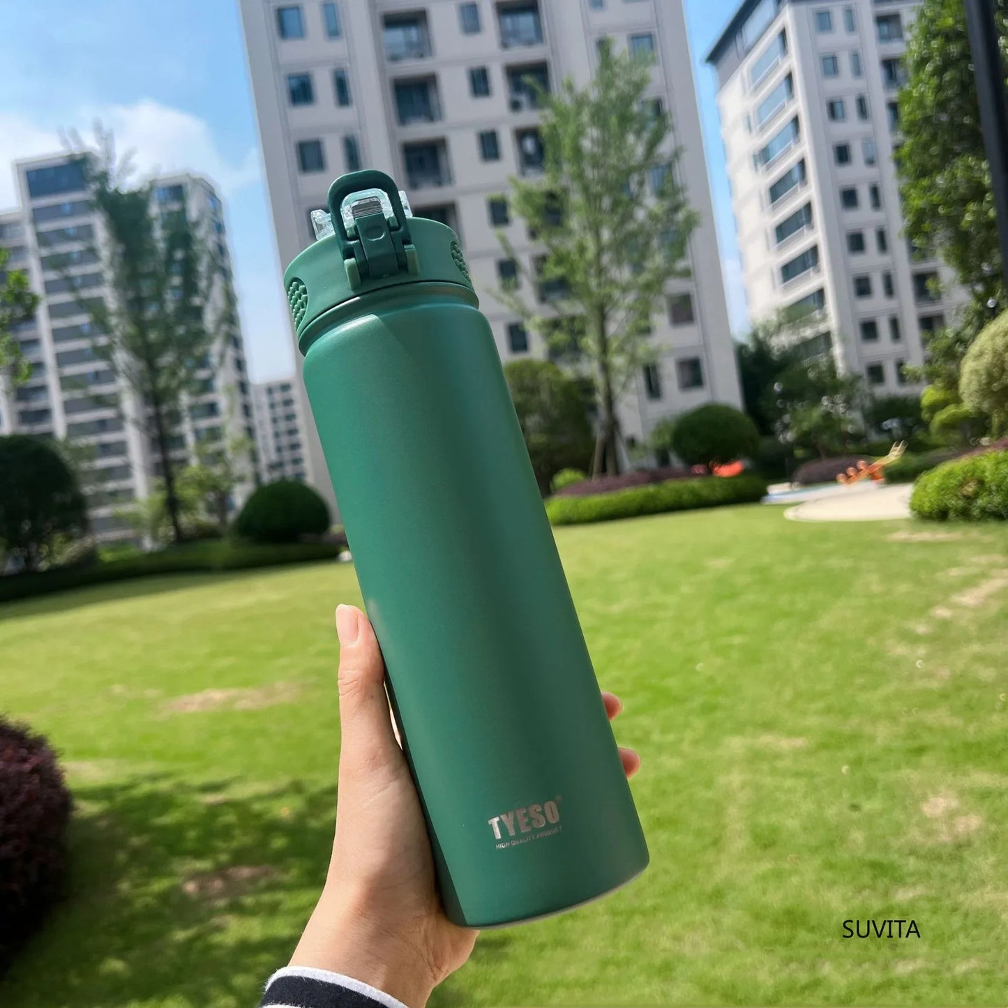 TYESO green thermos bottle with straw held in a garden. Double-wall insulated and BPA-free for hot or cold drinks.