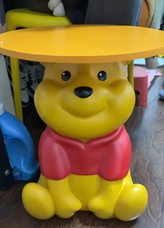 Whinnie the Pooh kidsYellow bear-shaped table with a red shirt on a wooden floor.