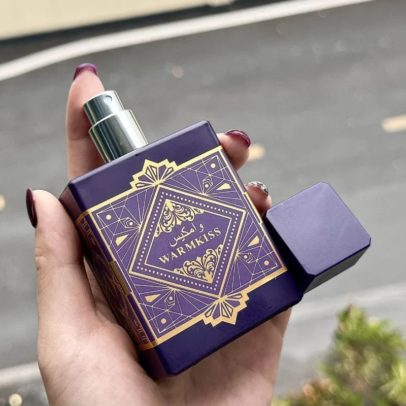Hand holding a purple and gold perfume bottle with 'WARMKISS' branding.