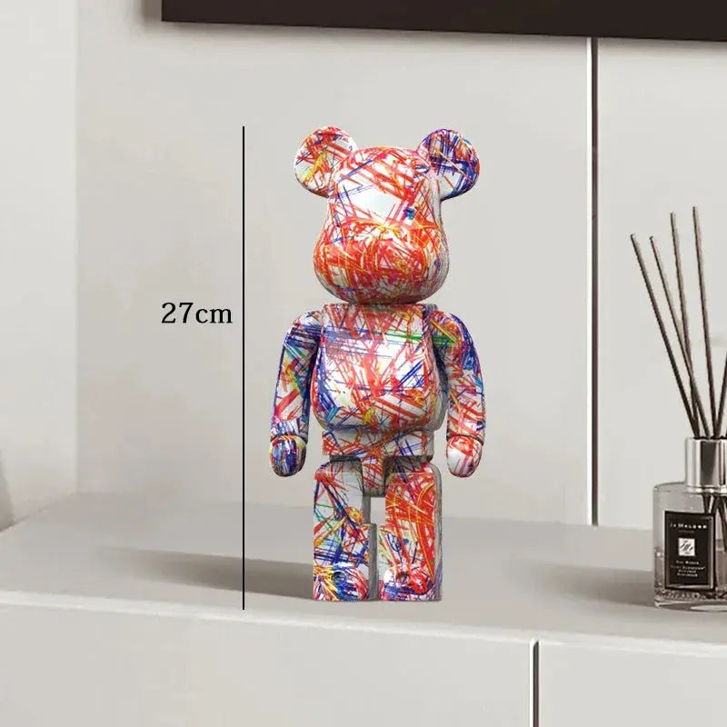 Colorful bear-shaped figure on a white surface with a vase in the background be@rbrick collectable