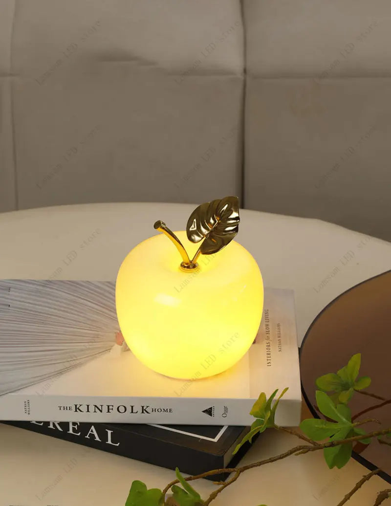 Decorative apple-shaped lamp on a stack of books with a neutral background