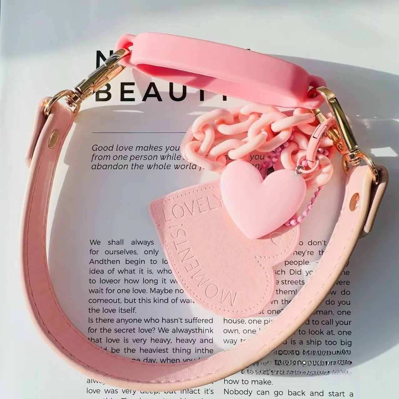 Pink handbag with decorative chain and heart charm on a magazine page