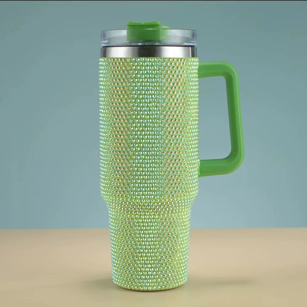 Green beaded tumbler with a handle on a beige surface and light blue background