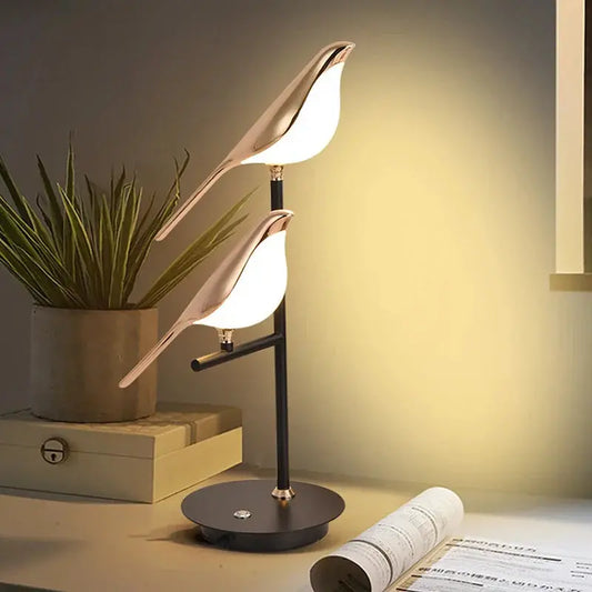 Modern table lamp with leaf design on a desk next to a plant and rolled-up paper.