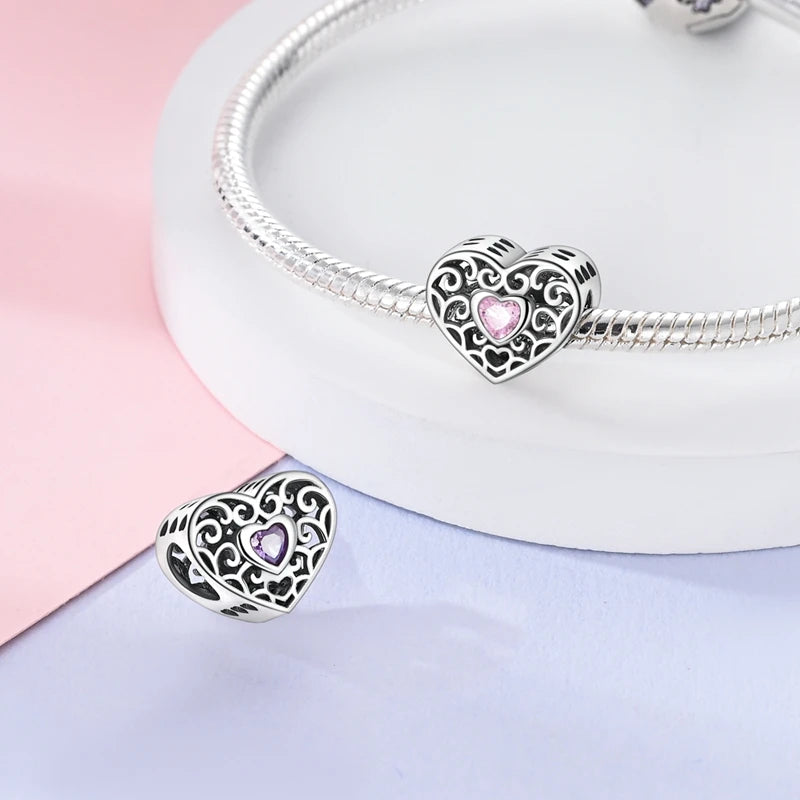 Heart-shaped silver charm with pink gem on a light pink and white background. pandora style