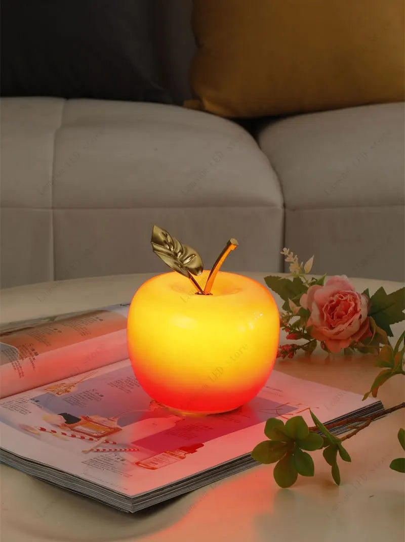 Apple-shaped night light on a magazine with flowers and a sofa in the background