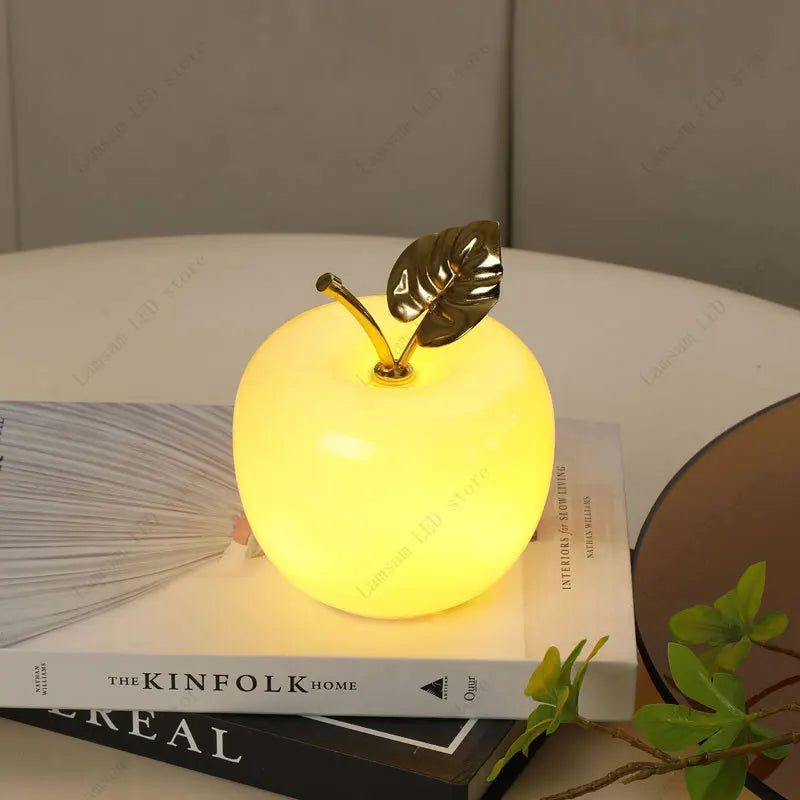 Yellow apple-shaped night light with a gold leaf on top, placed on books.