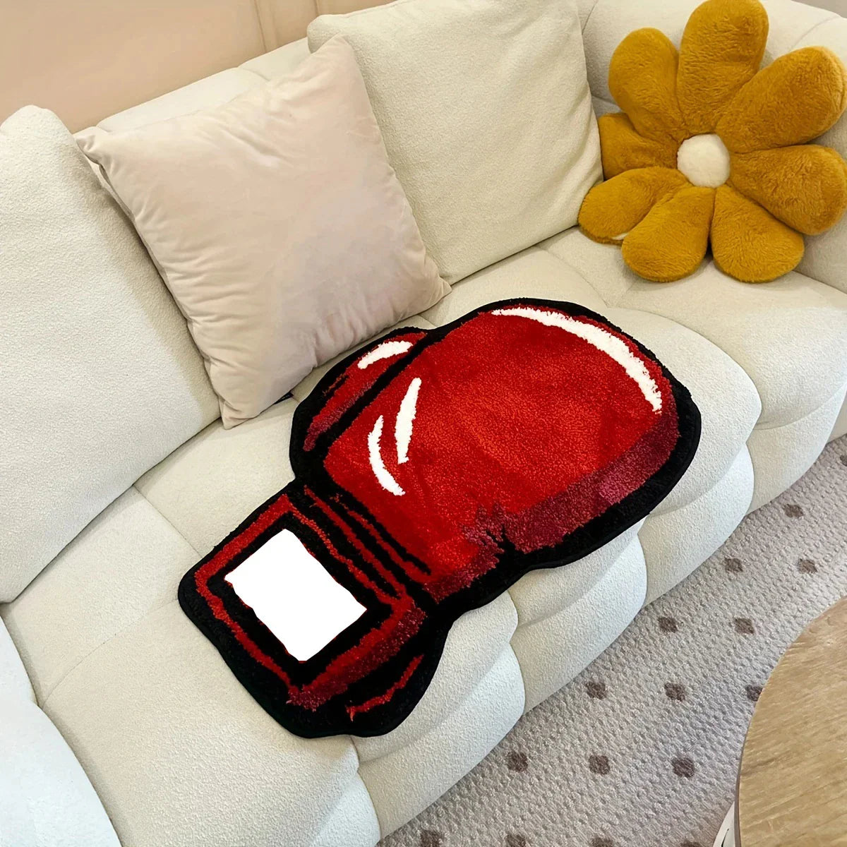 Red boxing glove-shaped rug on a beige sofa with decorative pillows.