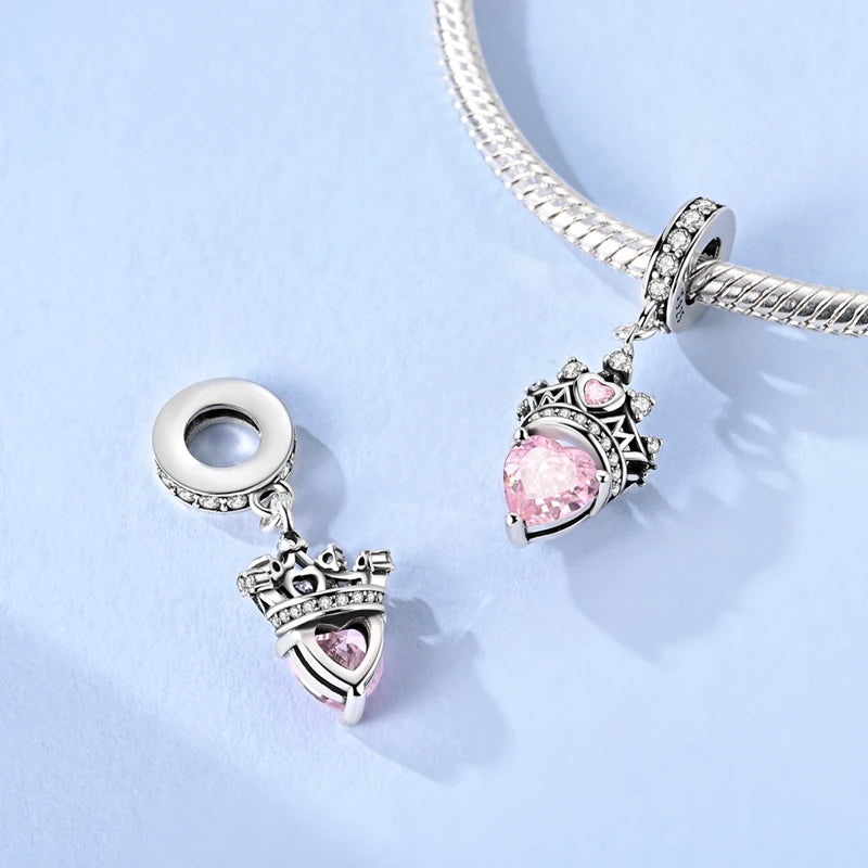 Two silver charms with pink gemstones on a light blue background. pandora style