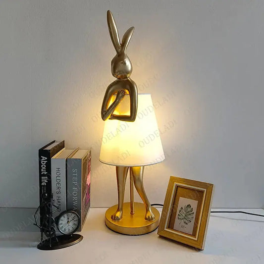 Gold rabbit-shaped lamp on a table with books and a clock.