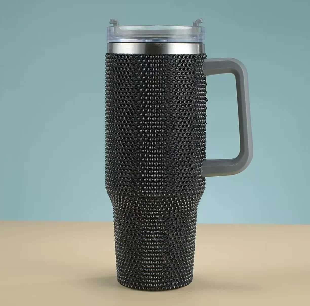Travel mug with black rhinestone embellishments on a beige surface with a light blue background