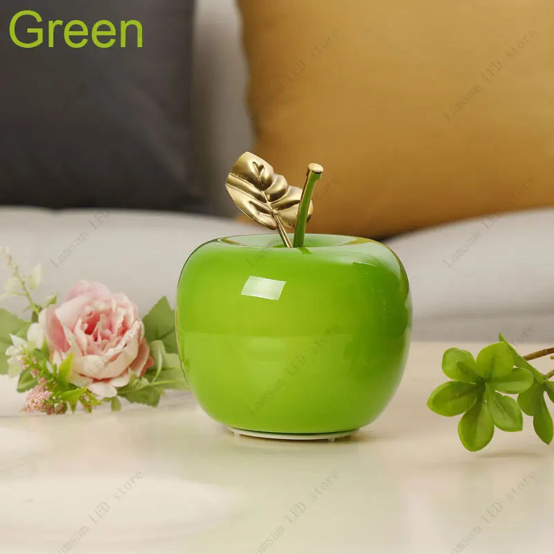 Decorative green apple with a gold leaf on a surface with flowers and a blurred background