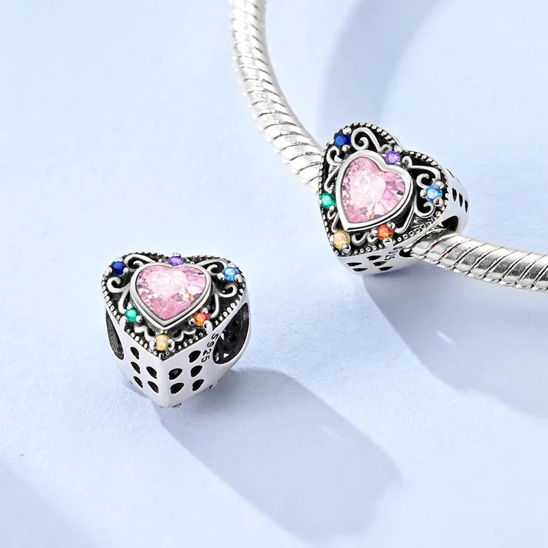 Heart-shaped jewelry charm with pink center and multicolored accents on a light blue background. pandora style