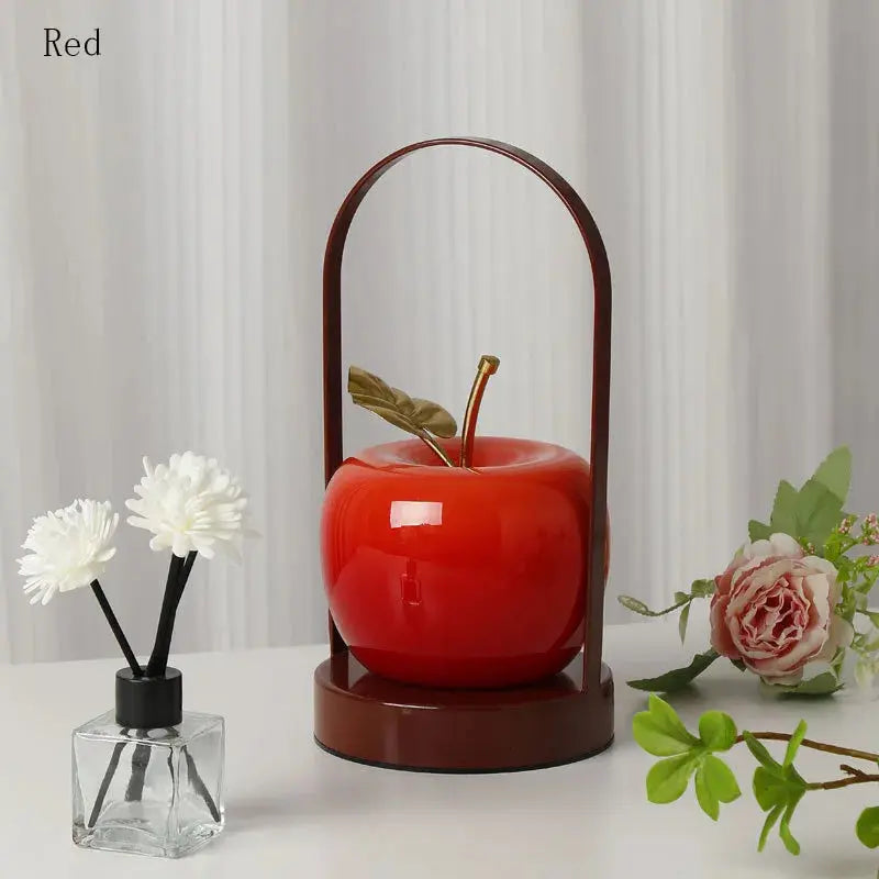 Decorative red apple with a brown stand on a white surface with flowers and a curtain background