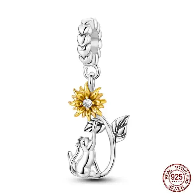 A sterling silver charm featuring a golden sunflower with green leaves on a heart-shaped base.