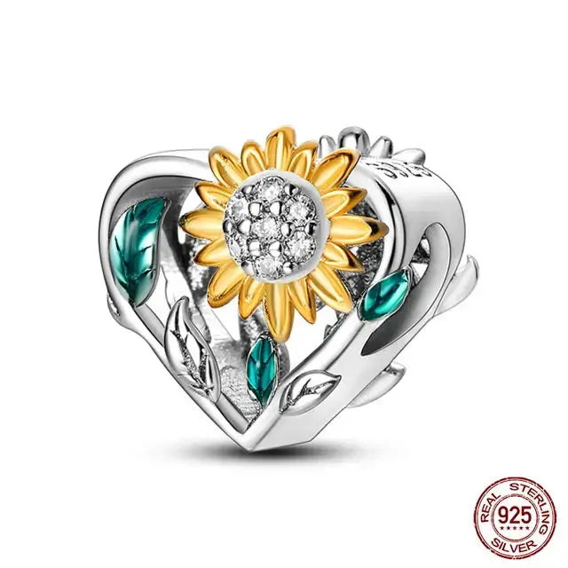 A sterling silver charm featuring a golden sunflower with green leaves on a heart-shaped base.