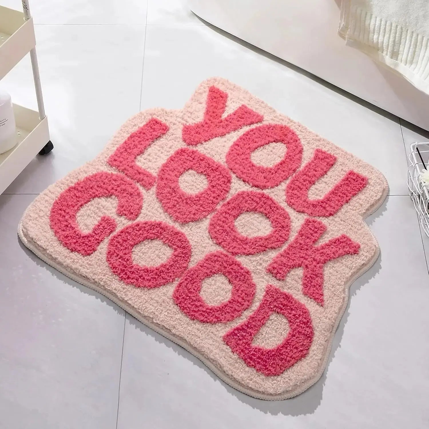 Pink and beige rug with 'YOU LOOK GOOD' text on a light gray floor. bath mat
