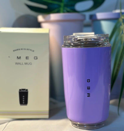 SMEG Purple mug with 'MEG' branding next to a beige box on a surface with plants in the background