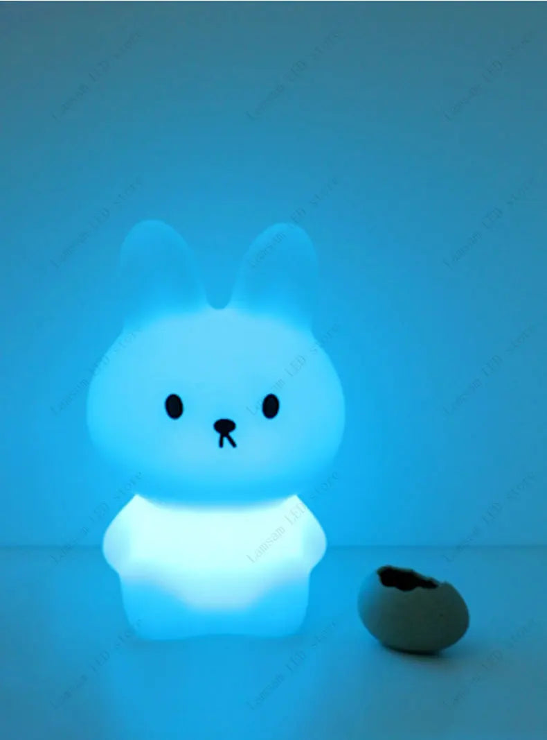 Cute cartoon-style rabbit night light glowing blue on a textured surface.