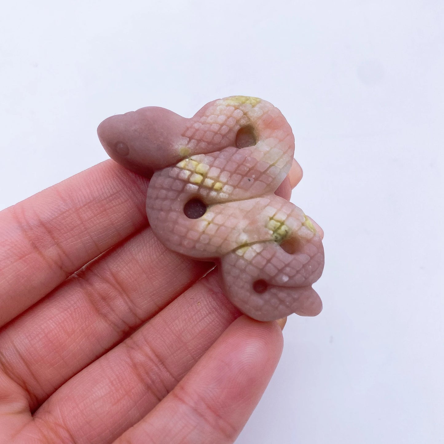 A collage of various crystal snake statues in different colors held in a person's hand.