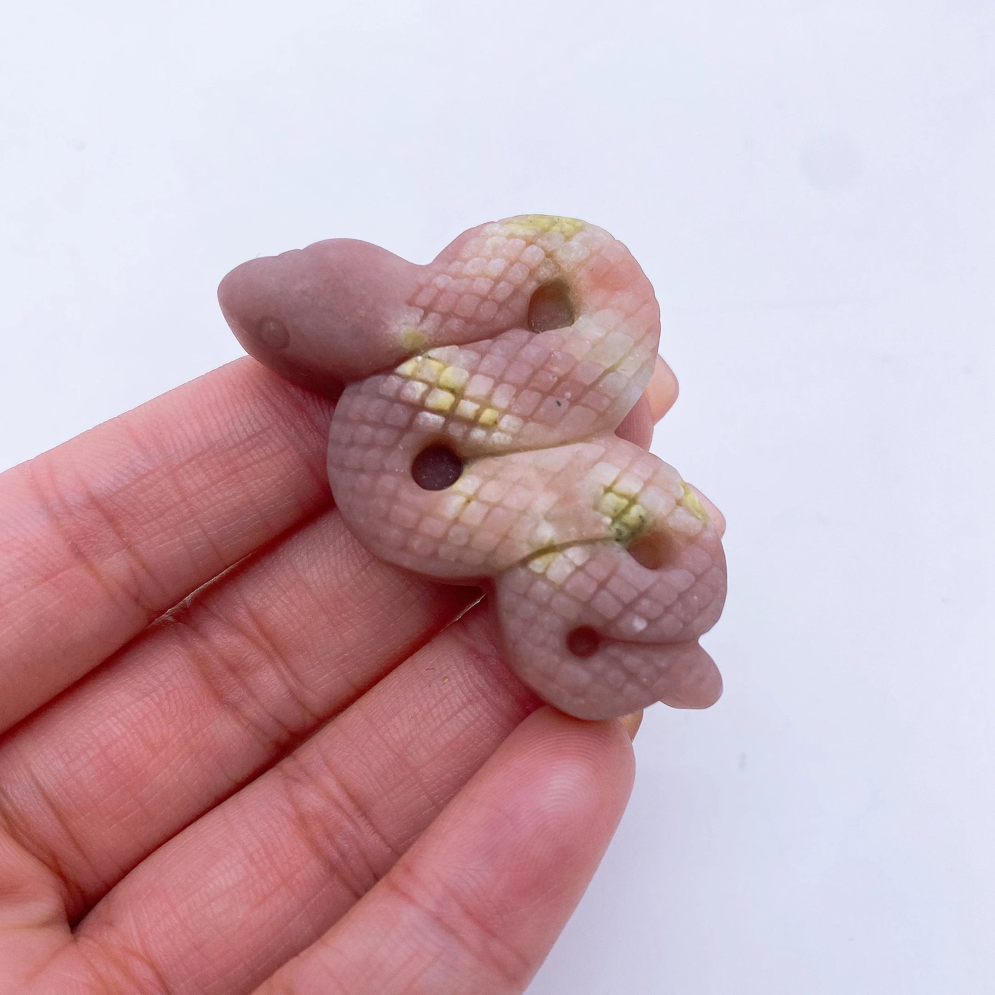 A collage of various crystal snake statues in different colors held in a person's hand.