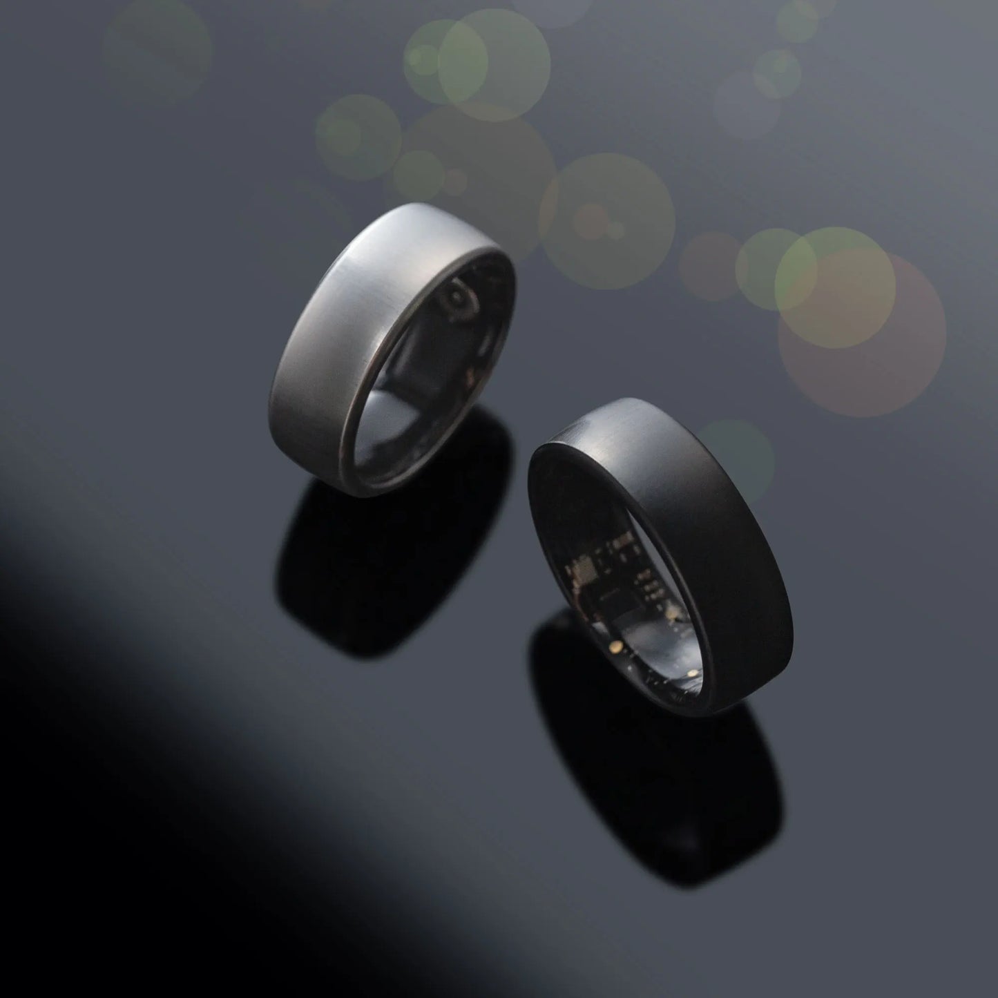 oura smart ring Two metallic rings on a reflective surface with a dark background