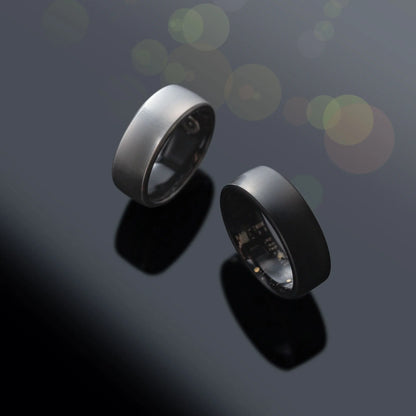 oura smart ring Two metallic rings on a reflective surface with a dark background